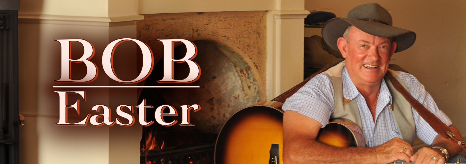 Bob Eater with guitar in front of fireplace.